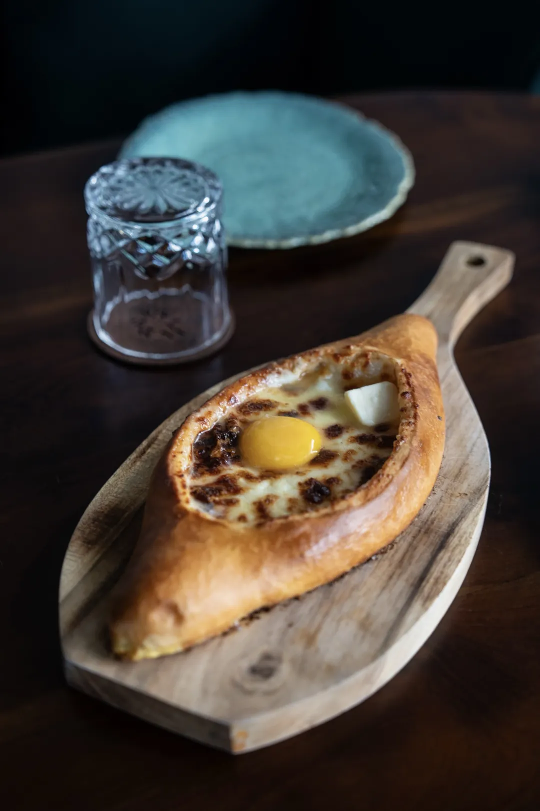 Khachapuri adjariano con yema y mantequilla sobre una tabla de madera en Tarragon, Uluwatu